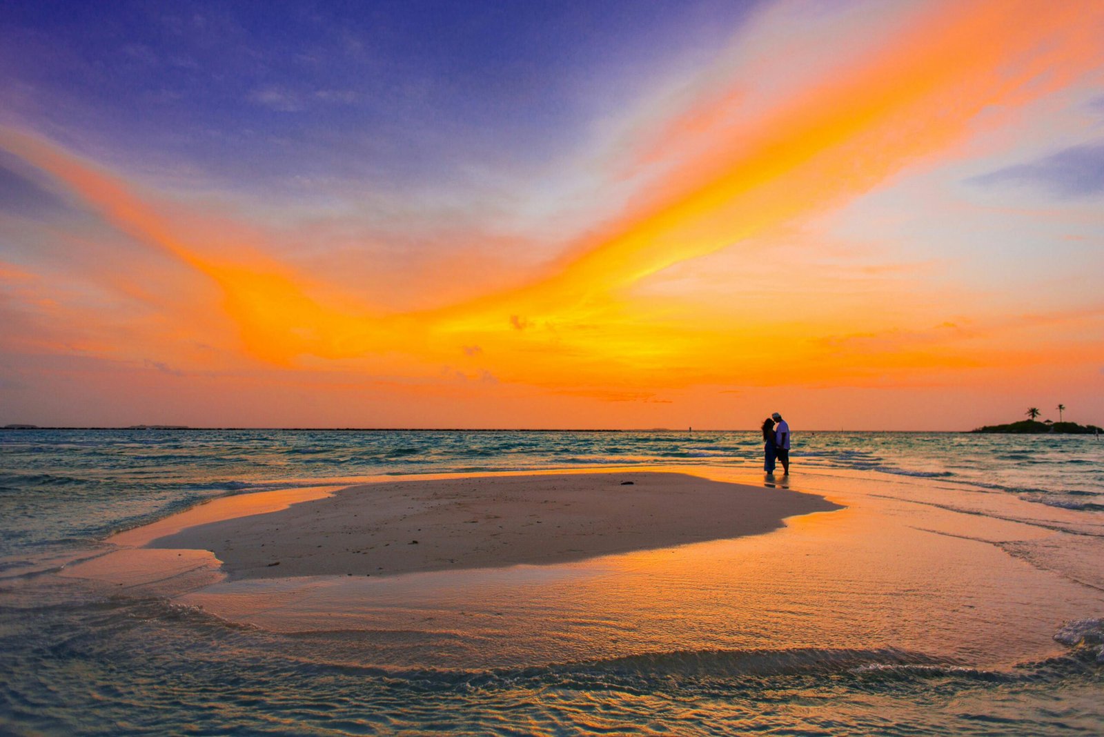 Tourism Couple shares a romantic moment on a serene tropical beach at sunset, surrounded by vibrant colors.