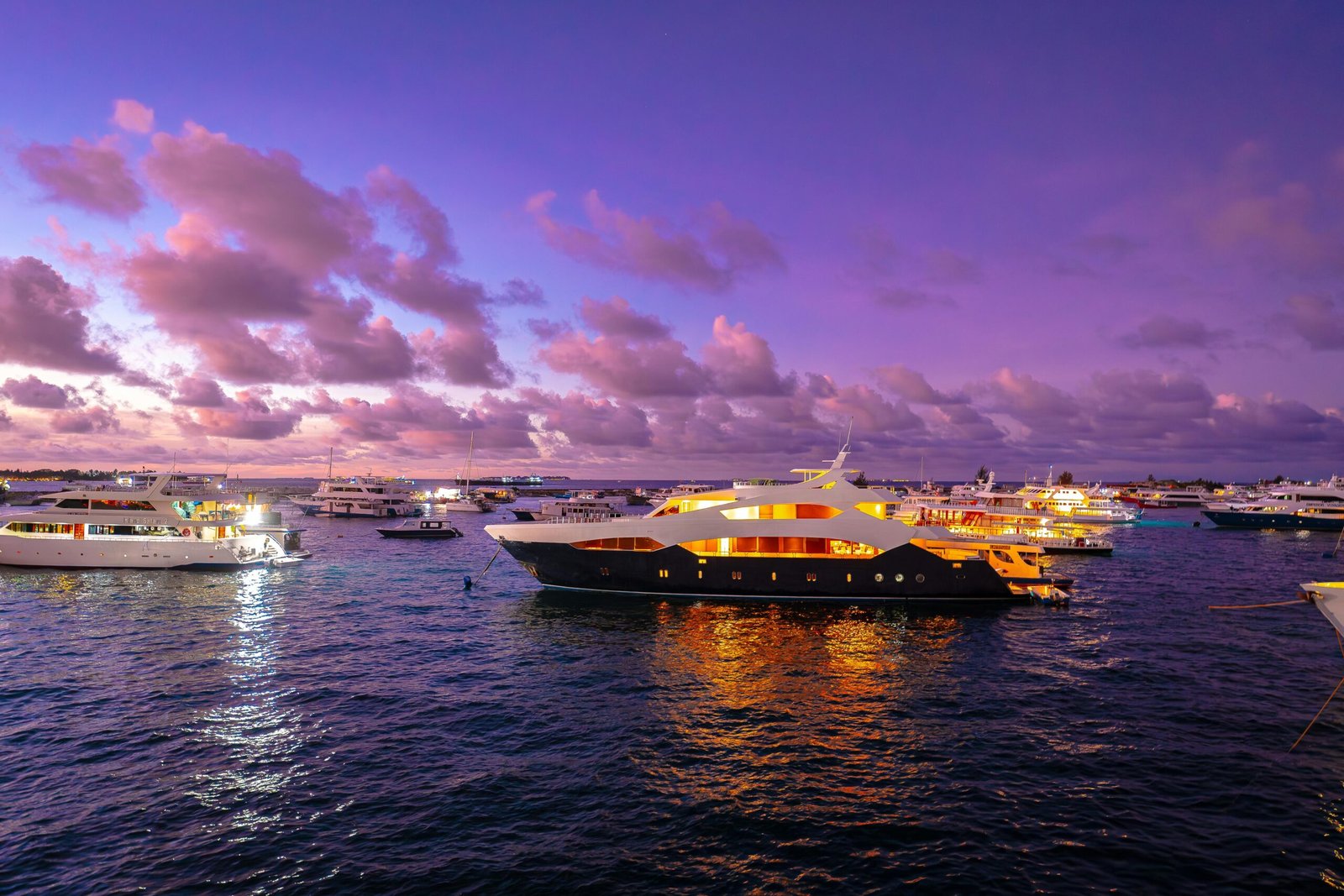 Tourism A scenic view of luxury yachts illuminated at sunset in the Maldives, offering a serene travel experience.