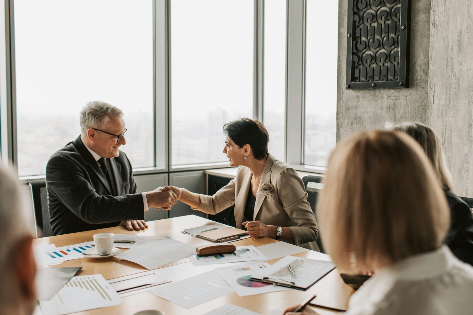 Immigration Colleagues in business attire shake hands during a formal meeting in a modern conference room.
