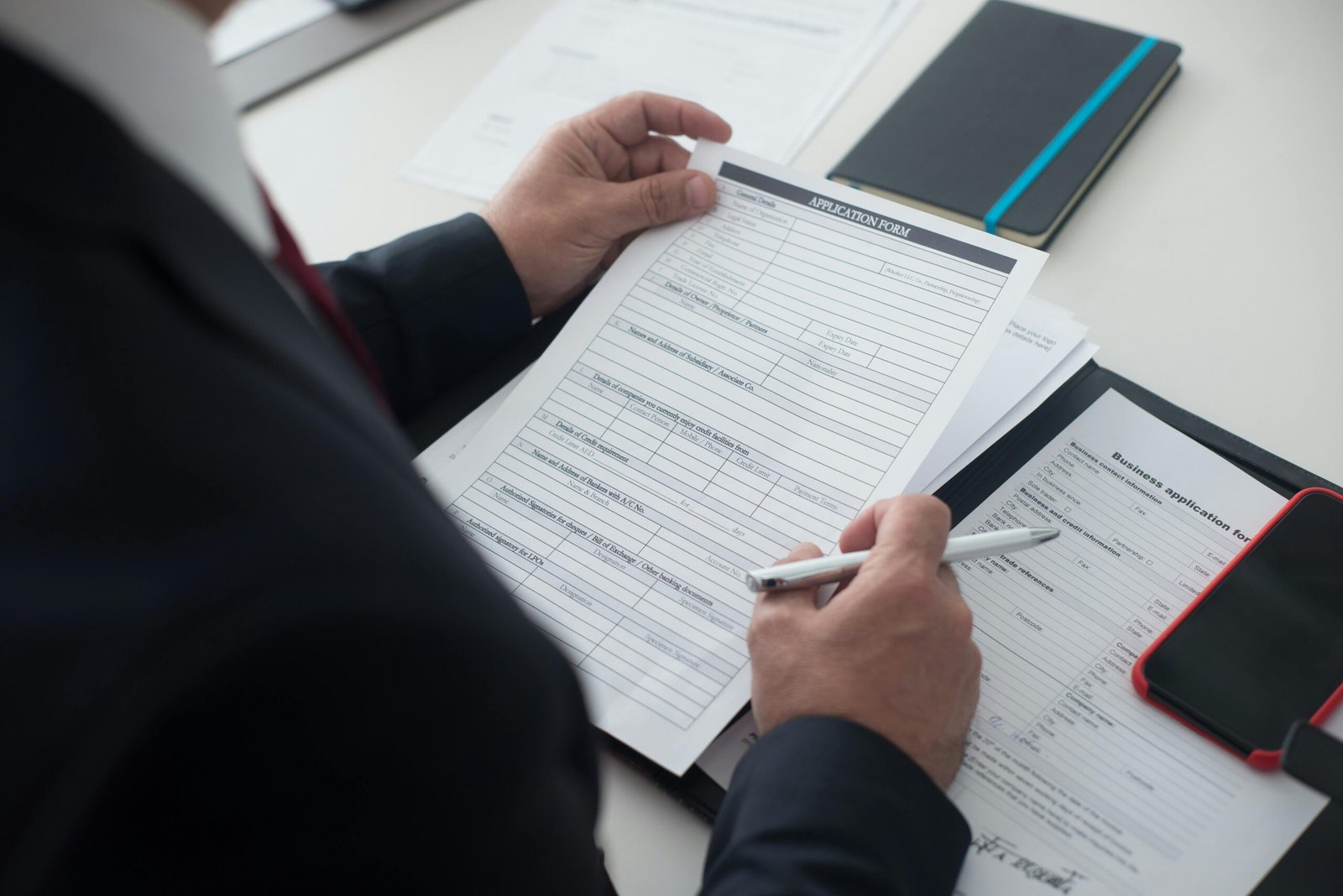 Immigration A businessman in a black suit reviews a printed application form with a pen on his desk.